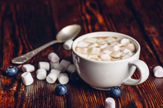 Cocoa Cup with Marshmallow with Scattered Few Blueberries and Some Marshmallows, and Spoon on Backdrop.