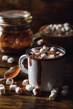 Metal Mug of Cocoa with Marshmallows. Jar of Cocoa Powder and Marshmallow Bowl on Backdrop. Vertical Orientation.