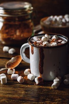 Mug of Cocoa with Marshmallows. Jar of Cocoa Powder and Marshmallow Bowl on Backdrop. Vertical Orientation.
