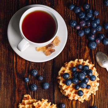 White Cup of Tea with Blueberries and Belgian Waffles on Wooden Background. View from Above.