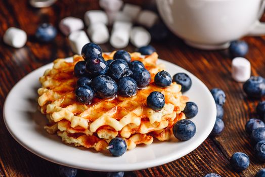 Belgian Waffles on Plate with Fresh Blueberry and Syrup. Some Berries and Marshmallow on Backdrop.