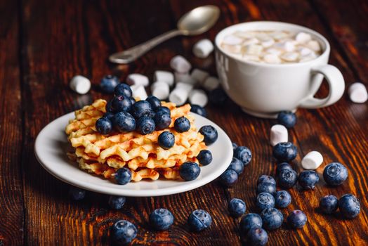 Belgian Waffles on Plate with Fresh Blueberry and Cup of Hot Cocoa with Marshmallow. Spoon and Some Berries and Marshmallows Scattered on Wooden Table.