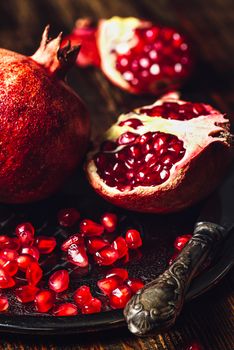 Opened Pomegranate and Whole One wiith Seeds on Metal Plate and Vintage Knife. Vertical Orientation.