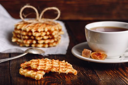 Breakfast with Waffles Stack on Napkin, White Cup of Tea and Pieces of Waffle on Wooden Surface.