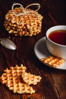 Waffles Pieces with White Cup of Tea and Stack of Waffles on Backdrop.