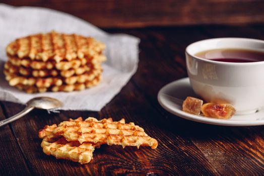 Breakfast with White Cup of Tea with Waffles Stack on Napkin and Pieces of Waffle on Wooden Surface.