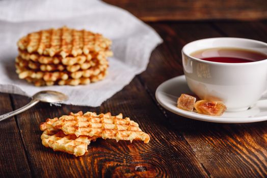 White Cup of Tea with Belgian Waffles Stack on Napkin and Pieces of Waffle on Wooden Surface.