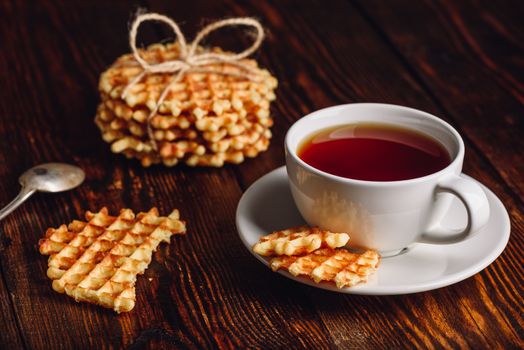 White Cup of Tea with Waffles Stack and Pieces of Waffle on Wooden Surface.