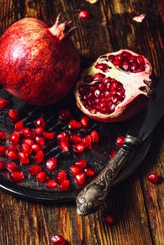 Opened Pomegranate and Whole One wiith Seeds on Metal Plate and Vintage Knife. Vertical Orientation.