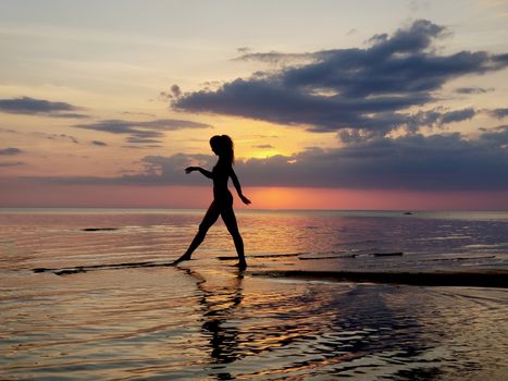 silhouette of a girl walking on the beach sand. Shooting against the sun. Sunset over the sea.