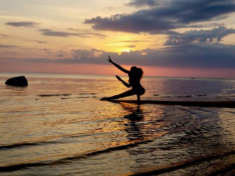 silhouette of a girl practicing yoga on the beach. Shooting against the sun. Sunset over the sea.