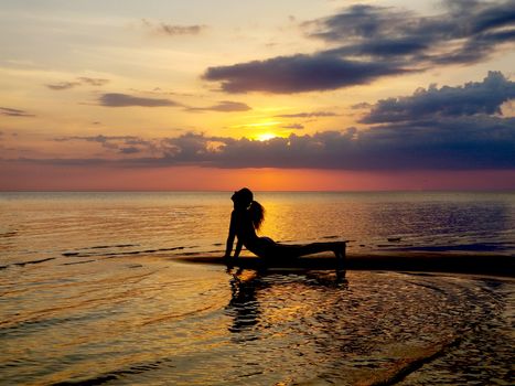 silhouette of a girl practicing yoga on the beach. Shooting against the sun. Sunset over the sea.