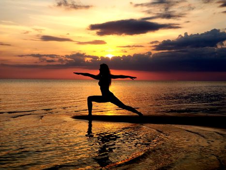 silhouette of a girl practicing yoga on the beach. Shooting against the sun. Sunset over the sea.