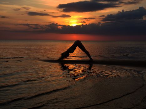 silhouette of a girl practicing yoga on the beach. Shooting against the sun. Sunset over the sea.