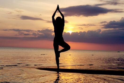 silhouette of a girl practicing yoga on the beach. Shooting against the sun. Sunset over the sea.