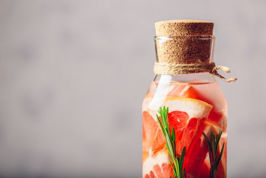 Bottle of Detox Water Infused with Sliced Raw Grapefruit and Fresh Springs of Rosemary. Copy Space on the Laft.