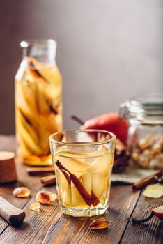 Infused Water in Glass and Bottle with Sliced Pear, Cinnamon Stick, Ginger Root and Some Sugar. Ingredients on Wooden Table. Vertical Orientation.
