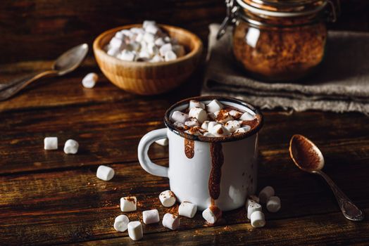Metal Mug of Cocoa with Marshmallows. Jar of Cocoa Powder and Marshmallow Bowl on Backdrop.