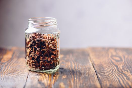 Jar of Star Anise Fruits and Seeds on Wooden Table. Copy Space on the Right.