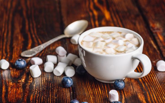 Cup of Coffee with Marshmallow with Scattered Few Blueberries and Some Marshmallows, and Spoon on Backdrop.