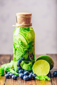 Bottle of Flavored Water with Lime, Mint and Blueberry and All Ingredients on Table. Vertical Orientation.