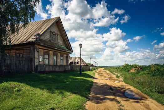 Traditional Wooden House for Russian Village. Dirt Road with Puddles.