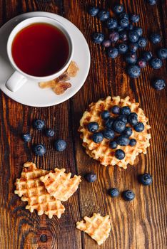 Cup of Tea with Blueberries and Whole and Broken Belgian Waffles on Wooden Background. Vertical Orientation.