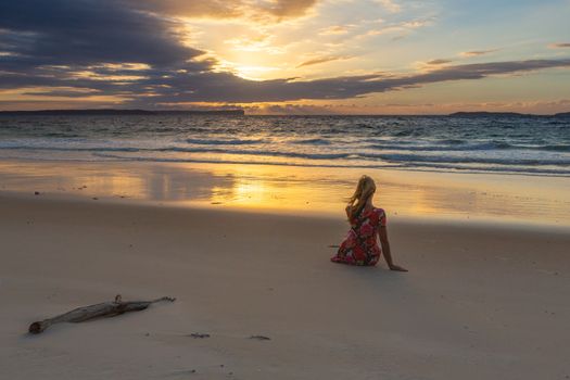 Female sitting on the beach and watching the beautiful sunrise, so tranquil