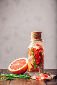Bottle of Infused Water with Sliced Grapefruit and Fresh Springs of Rosemary. Ingredients and Knife on Wooden Table. Vertical Orientation. Copy Space on the Top.