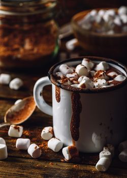 Dirty Mug of Cocoa with Marshmallows. Jar of Cocoa Powder and Marshmallow Bowl on Backdrop. Vertical Orientation.