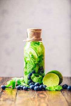 Bottle of Infused Water with Lime, Mint and Blueberry and All Ingredients on Table. Copy Space and  Vertical Orientation.