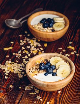 Two Bowl of Muesli with Banana, Blueberry and Greek Yogurt for Breakfast. Scattered Granola on Wooden Table. Vertical Orientation.