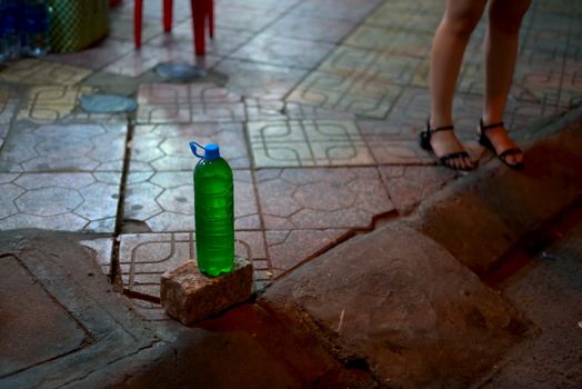 PET bottle full of gasoline for sale placed on top of a pavement on the sidewalk in Vietnam at night.