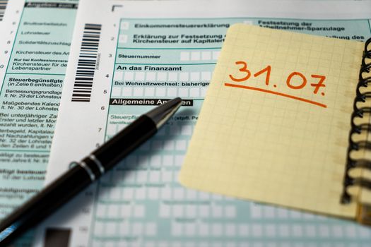 German tax declaration form with a black pen in foreground and a yellow paper indicating the deadline of the 31st of july.