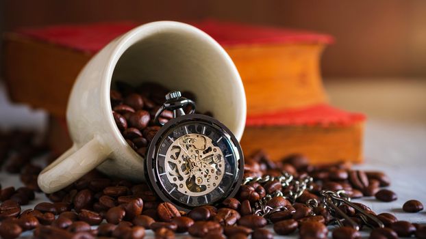 Pocket watch and coffee cup on coffee seed and old book on wooden table. Copy space for text. The concept of time to read books.
