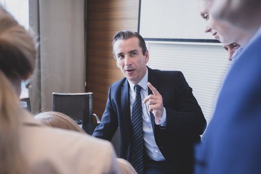 Leadership and communication. Business speech. Handsome mid adult man in suit talking to his colleagues - group of people at meeting table