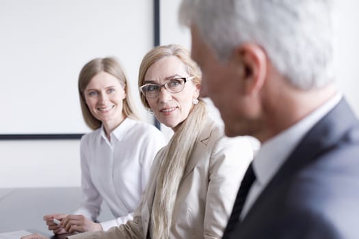 Business people sitting in a row and working, focus on mature woman in glasses