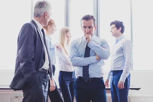 Colleagues having business conversation at meeting in office, serious man thinking holding chin