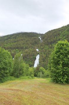 Beautiful landscape with waterfall mountains forest and meadow in summer Norway