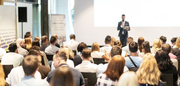 Male speaker giving a talk in conference hall at business event. Audience at the conference hall. Business and Entrepreneurship concept. Focus on unrecognizable people in audience.