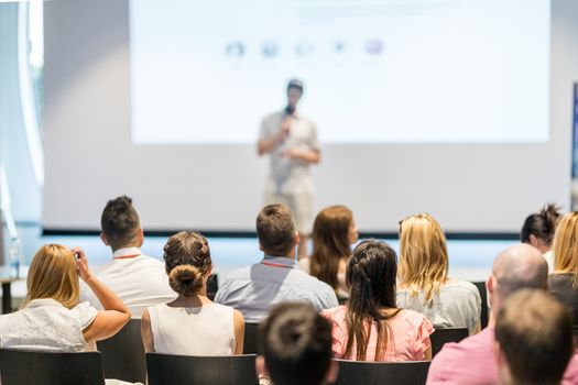 Male speaker giving a talk in conference hall at business event. Audience at the conference hall. Business and Entrepreneurship concept. Focus on unrecognizable people in audience.