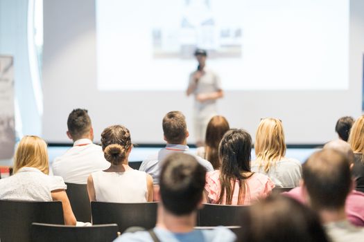 Male speaker giving a talk in conference hall at business event. Audience at the conference hall. Business and Entrepreneurship concept. Focus on unrecognizable people in audience.