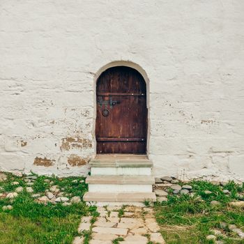 Old, Brown, Wooden Door on White Brick Wall with Stone Path and Grass