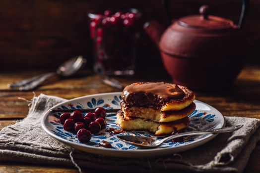 Quark Pancakes with Chocolate Topping, Frozen Cherry and Vanilla Pod. Tea Pot with Spoons and Glass of Berries on Background.