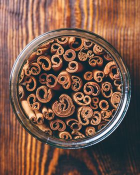 Jar of Cinnamon Sticks over wooden background. View from above.