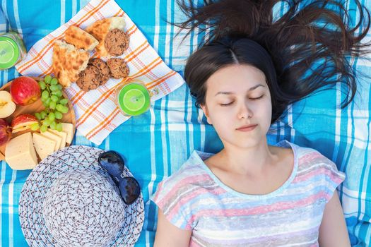 Young girl with long dark hair is lying on a plaid on a picnic on a summer day - summer holidays and vacation concept.