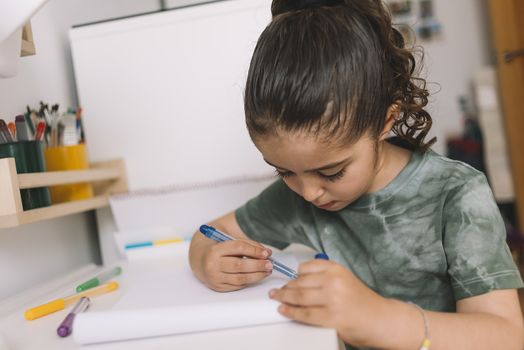 little girl draws at home with colored markers, she is drawing on the desk in her room