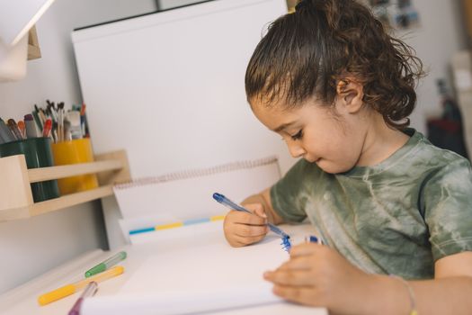 little girl drawing at home with colored markers, she is drawing on the desk in her room