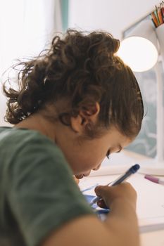 vertical photo of a little girl drawing concentrated at home with color marker, she is drawing on the table in her room