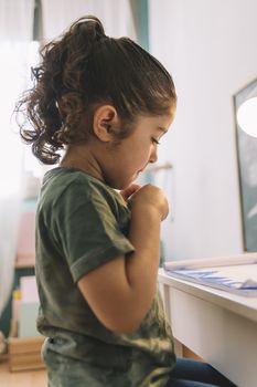 vertical photo of a little girl looking at the draw she just made at home with color markers, the draw is on the desk in her room